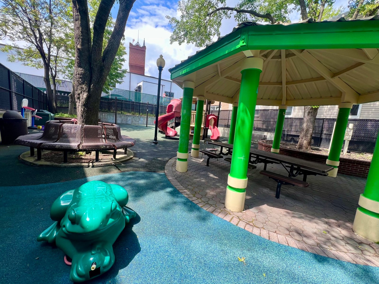 small park with frog sprinkler and playground with water tower in background